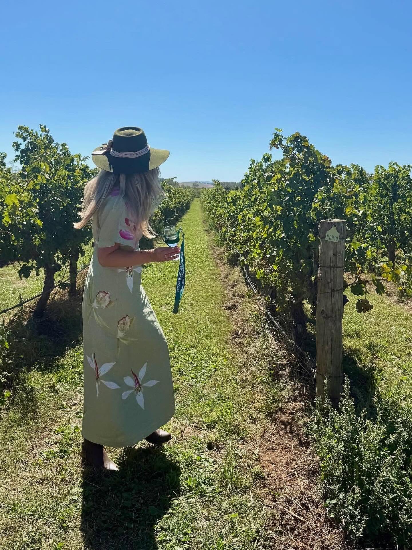 Jen standing between vineyard rows in Orange with a glass of wine