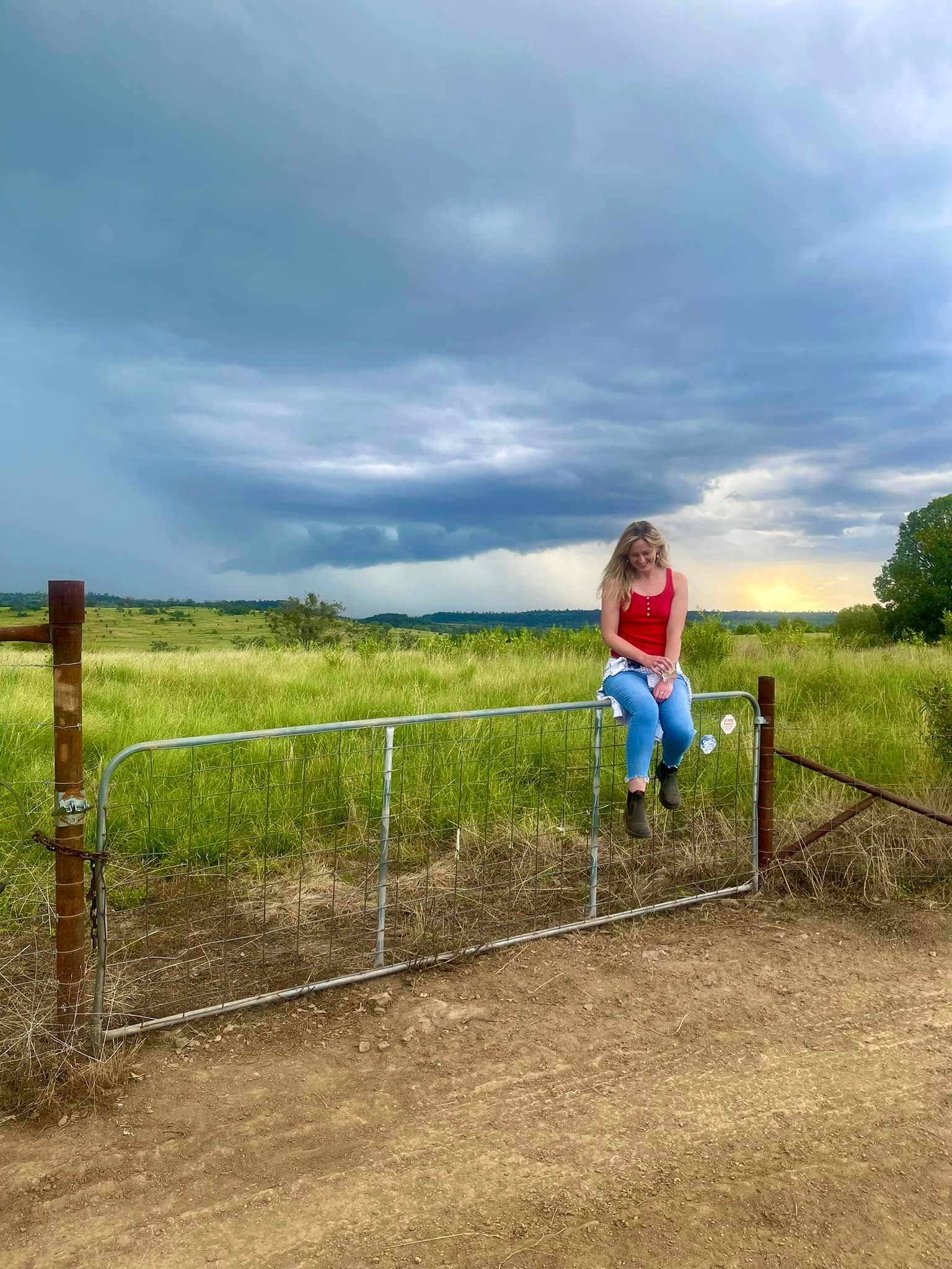 Jen sitting on a gate with dramatic skies in regional New South Wales